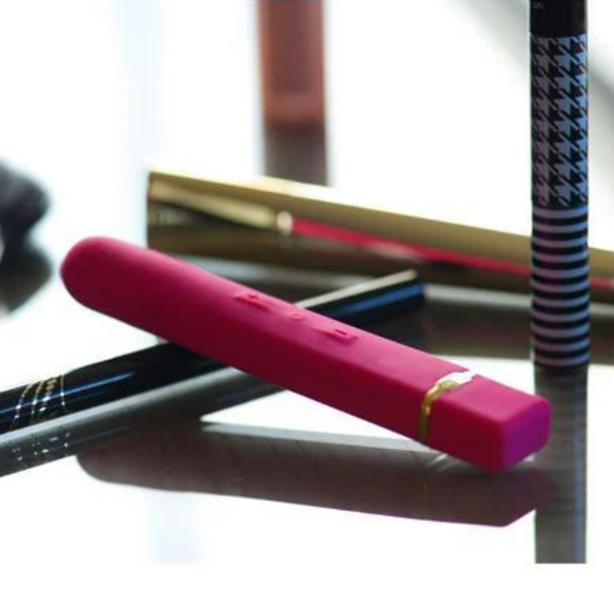Pink rechargeable silicone vibrator resting beside make up tools